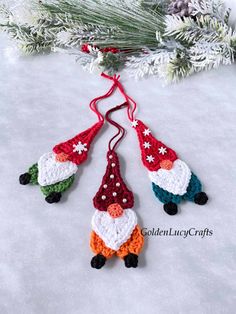 three crocheted christmas ornaments hanging from a pine branch on top of snow covered ground