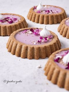 four small desserts with purple icing and white frosting on top are arranged in the shape of tarts