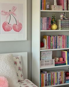 a white book shelf filled with lots of books next to a pink and yellow chair