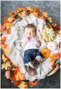 a baby is laying down on a blanket surrounded by fall leaves and pumpkins