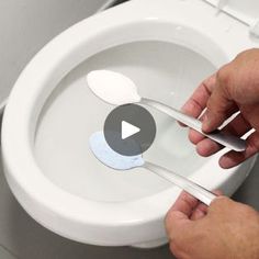 a person holding two spoons over a toilet bowl with the lid up and an object stuck to it