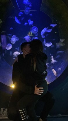 two people are hugging in front of a jelly fish tank at the aquarium with blue lights