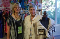 two women standing next to each other in front of some clothes on display at a store