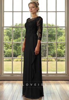 a woman standing in front of a window wearing a long black dress with sheer sleeves