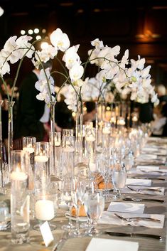 a long table with candles and flowers in vases on top of it, along with place settings