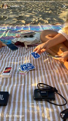 a woman sitting on top of a beach towel next to a bag and cell phone