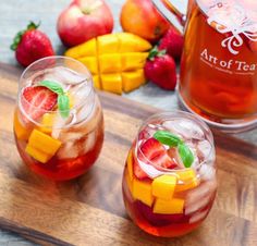 two glasses filled with fruit and ice sitting on top of a wooden cutting board next to apples