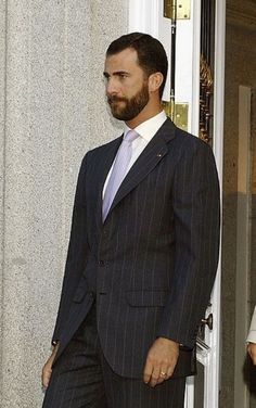 a man in a suit and tie walking out of a door with another man standing behind him