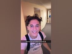 a young man with curly hair and suspenders smiles at the camera while standing in an office hallway