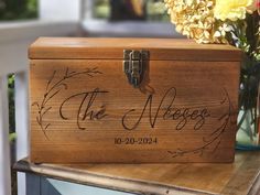 a wooden box sitting on top of a table with flowers in the vase behind it