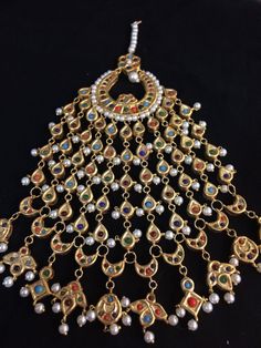 an ornate gold necklace with pearls and stones on the bottom, hanging from a black background