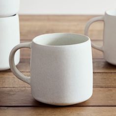 two white coffee mugs sitting on top of a wooden table next to each other