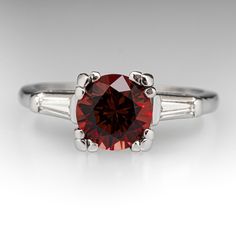 This lovely vintage ring is centered with one (1) round brilliant cut natural rhodolite garnet set into a four-prong setting. The shoulders of the ring are each accented with one (1) channel set, tapered baguette cut diamond. The ring measures 7.6mm at the top, rises 8.1mm above the finger, tapering to 1.2mm wide and 1.1mm thick at the base of the shank. It is currently a size 6.25. Fine Jewelry Garnet Rings With Brilliant Cut, Garnet Rings In Brilliant Cut Fine Jewelry, Garnet Rings With Brilliant Cut In Fine Jewelry Style, Elegant Garnet Ring With Prong Setting, Garnet Rings With Brilliant Cut Fine Jewelry, Elegant Garnet Round Cut Rings, Elegant Garnet Ring With Center Stone, Timeless Red Rings With Brilliant Cut, Red Classic Birthstone Ring With Prong Setting