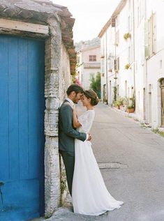 a bride and groom are kissing in front of a blue door on a cobblestone street