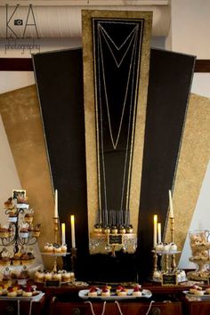 a table topped with lots of desserts next to a tall black and gold wall