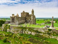 an old castle sits on top of a grassy hill in the middle of a green field