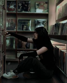 a woman sitting on the floor in front of a book shelf