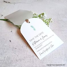 a white wedding card with flowers on the side and a tag that says save the date