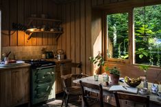 a kitchen with an oven, table and chairs next to a window that looks out onto the woods