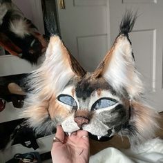 a cat mask being held up to the camera by someone's hand with blue eyes