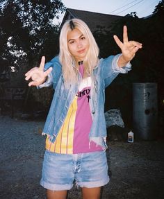 a woman with blonde hair wearing a blue jean jacket and holding her hands up in the air