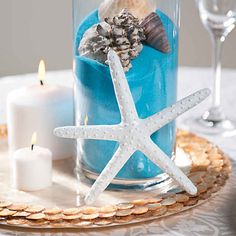 a starfish and seashells in a glass container on a tray with candles