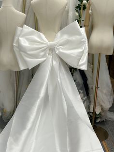 two mannequins with white bows on them in front of some wedding dresses