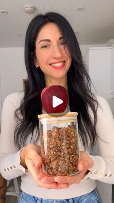 a woman is holding an apple in a jar with granola inside and the video below