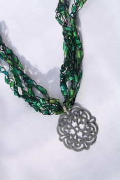 a necklace with green beads and a metal medallion on it's end is shown