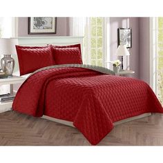 a bed with red bedspread and pillows in a room next to a window