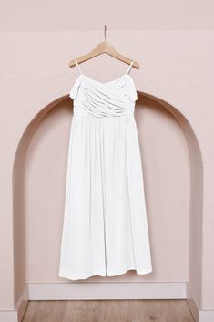 a white dress hanging on a wooden hanger in front of a pink wall and wood floor