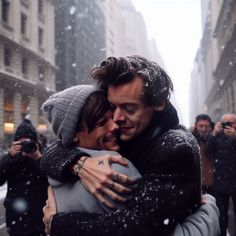 two people hugging each other in the middle of a city street with snow falling all around them