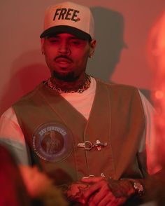 a man wearing a hat and vest standing in front of a red light with his hand on his hip