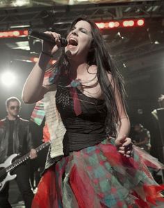 a woman singing into a microphone while holding a guitar in her hand and wearing a colorful dress