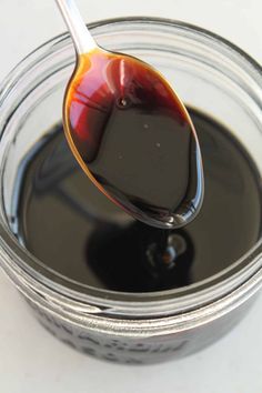 a spoon full of black liquid sitting on top of a jar filled with brown liquid