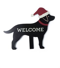 a black dog with a santa hat on it's head is standing in front of a sign that says welcome