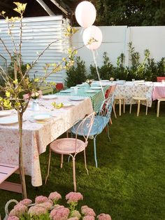 an outdoor dining area with tables, chairs and balloons on the table in the grass