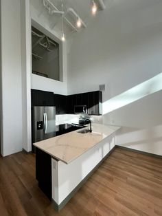 an empty kitchen with white counter tops and black cabinets, along with hardwood floors in the middle