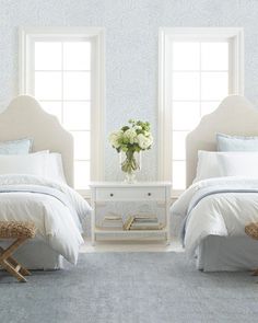 two white beds in a bedroom with blue and white wallpaper on the walls behind them