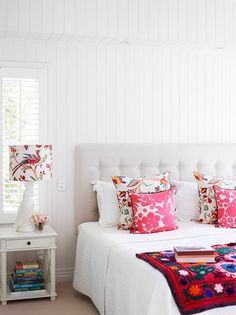 a white bed topped with lots of pillows next to a night stand and window sill