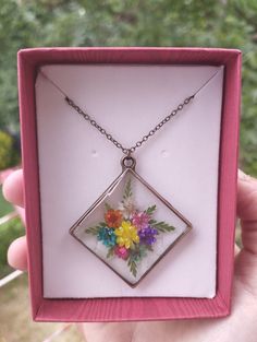 a pink box holding a necklace with flowers in it and a chain hanging from the front