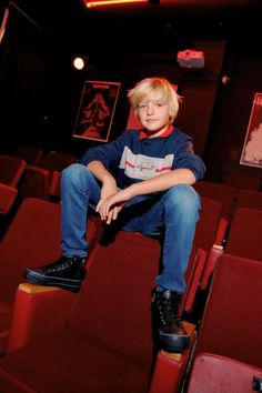 a young boy sitting on top of a red chair in a movie theater with his legs crossed