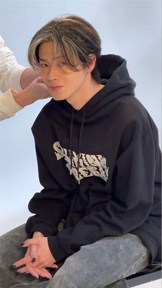 a young man sitting on top of a skateboard wearing a black hoodie and jeans