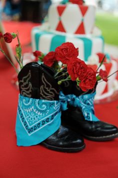 a pair of cowboy boots sitting on top of a red tablecloth covered floor next to a cake