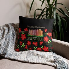 a black pillow with red flowers on it sitting on a couch next to a potted plant