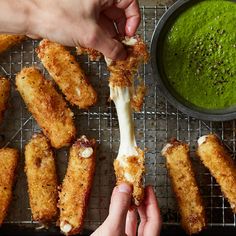 several fried food items on a cooling rack next to a bowl of pesto sauce