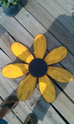 a yellow flower sitting on top of a wooden floor next to a person's feet