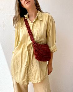 a woman is wearing a yellow shirt and holding a red crocheted purse in her hands