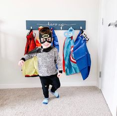 a little boy standing in front of a coat rack with clothes hanging on it's hooks