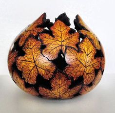 a vase with leaves painted on it sitting on a white tableclothed surface, in the shape of a ball